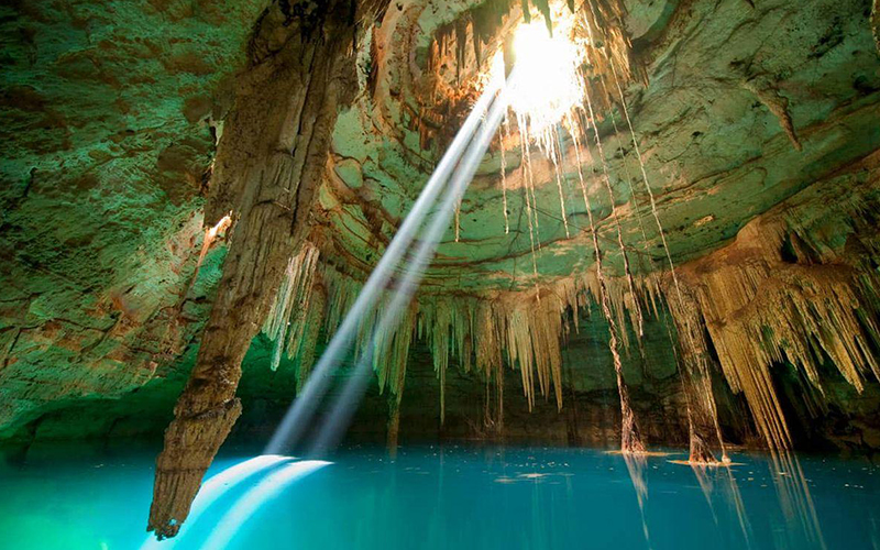Cave cenote in the Riviera Maya with natural sun rays shining into crystal-clear water.