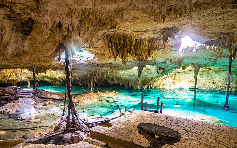 Interior of a cave cenote in the Riviera Maya with rock formations and crystal-clear water.
